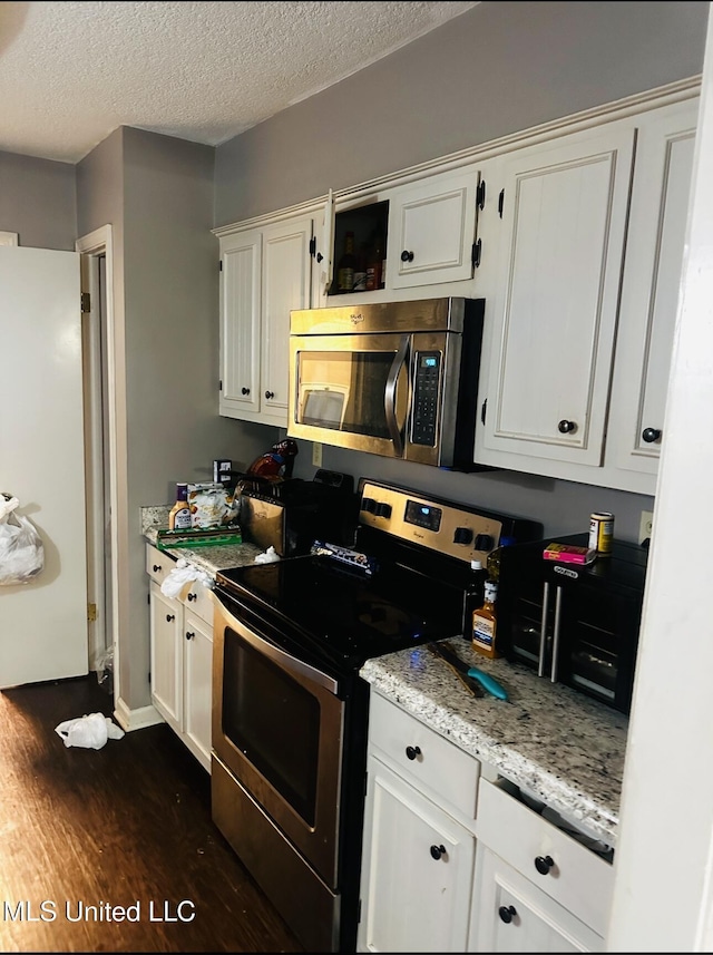 kitchen with light stone counters, dark wood-style flooring, stainless steel appliances, white cabinets, and a textured ceiling