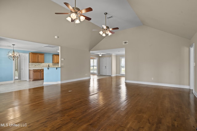 unfurnished living room with visible vents, high vaulted ceiling, ceiling fan with notable chandelier, wood finished floors, and baseboards