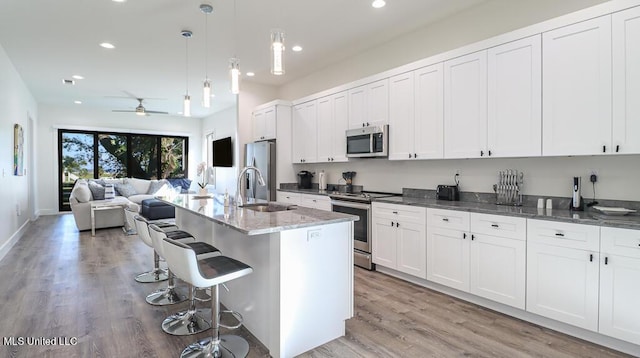 kitchen with a kitchen bar, stainless steel appliances, ceiling fan, a kitchen island with sink, and pendant lighting