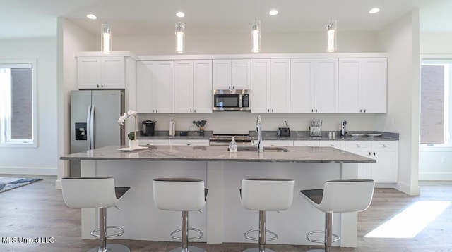 kitchen featuring dark stone countertops, an island with sink, hanging light fixtures, and appliances with stainless steel finishes