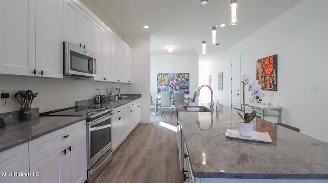 kitchen with sink, stainless steel appliances, a large island with sink, dark stone countertops, and pendant lighting