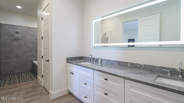 bathroom with hardwood / wood-style flooring, vanity, and a tile shower