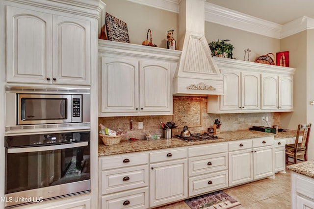 kitchen featuring crown molding, appliances with stainless steel finishes, light stone counters, light tile patterned floors, and backsplash