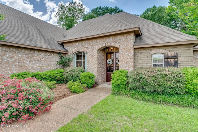view of exterior entry featuring brick siding and roof with shingles