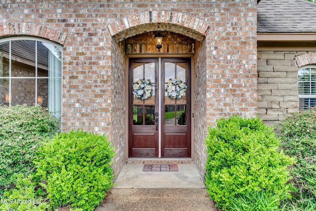 entrance to property with french doors, a shingled roof, and brick siding