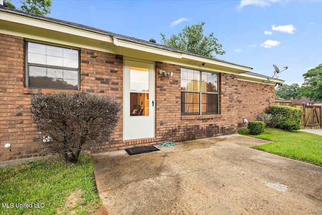 view of exterior entry with brick siding, a patio area, and fence