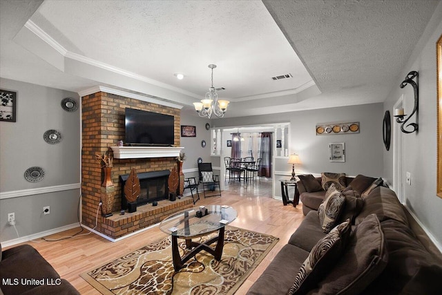 living area featuring a textured ceiling, light wood-type flooring, a chandelier, a brick fireplace, and a tray ceiling