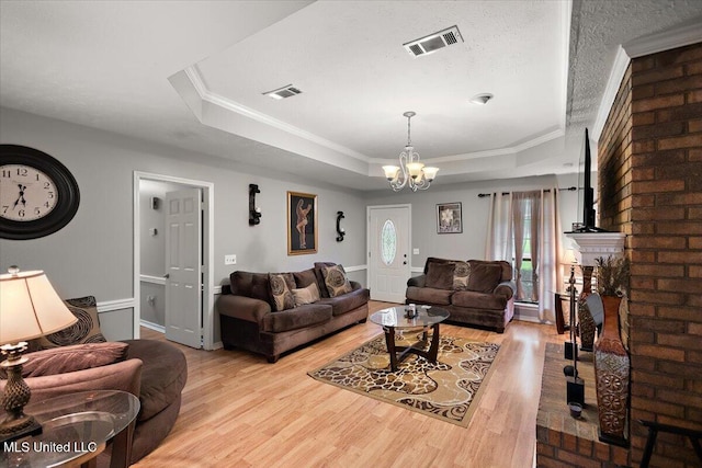 living area featuring a raised ceiling, light wood-type flooring, a chandelier, crown molding, and baseboards