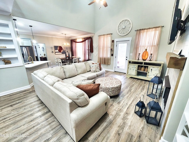 living room with a towering ceiling, crown molding, ceiling fan with notable chandelier, and light hardwood / wood-style floors