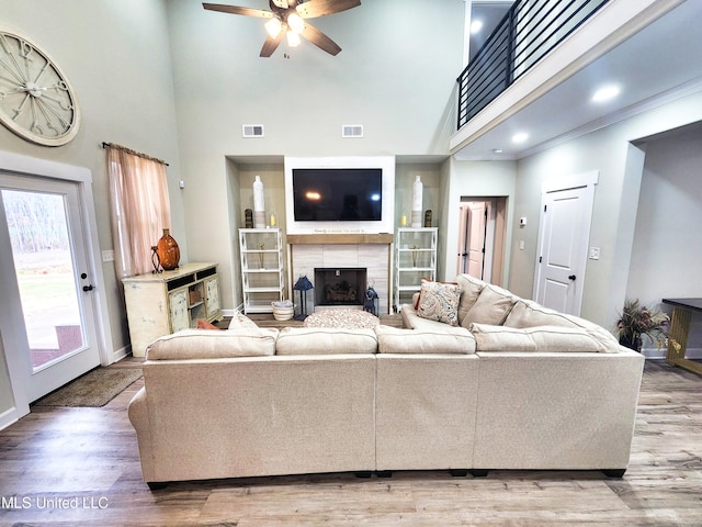 living room featuring hardwood / wood-style flooring, a tiled fireplace, a high ceiling, and ceiling fan