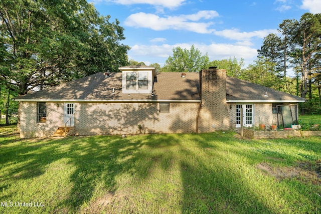 back of house with brick siding, a shingled roof, a yard, and a chimney