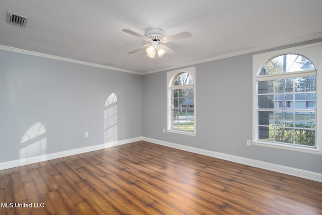 empty room with ornamental molding, wood finished floors, visible vents, and baseboards