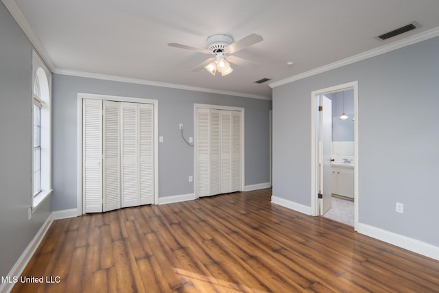 unfurnished bedroom with wood finished floors, two closets, visible vents, and crown molding