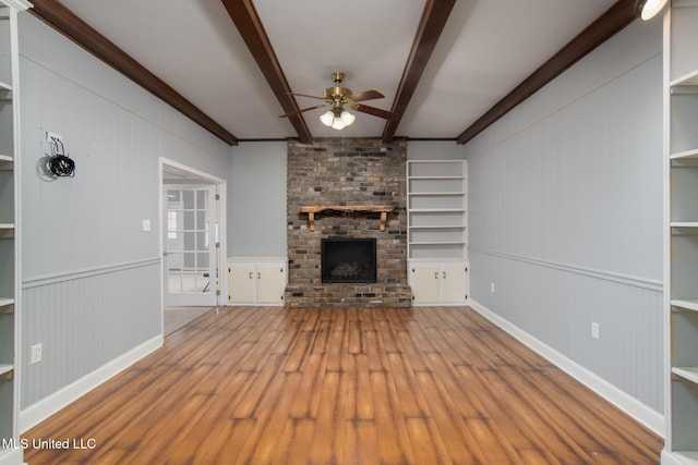 unfurnished living room featuring a ceiling fan, a brick fireplace, beamed ceiling, and wood finished floors