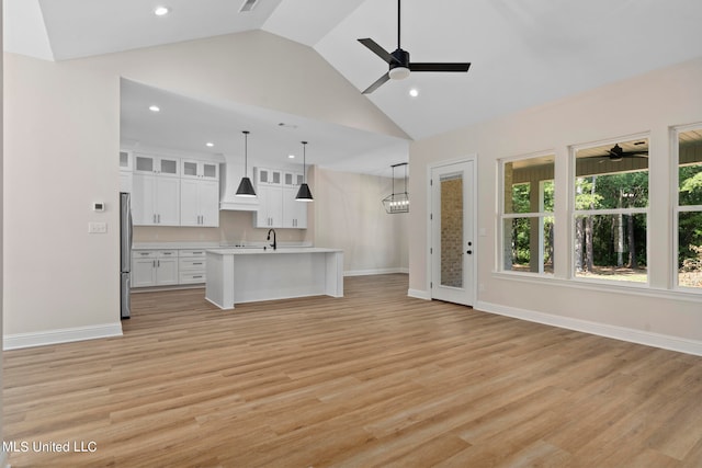 unfurnished living room featuring light hardwood / wood-style floors, high vaulted ceiling, sink, and ceiling fan with notable chandelier