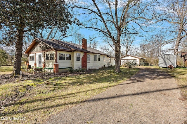 view of front facade featuring a front yard, driveway, an outdoor structure, and a chimney