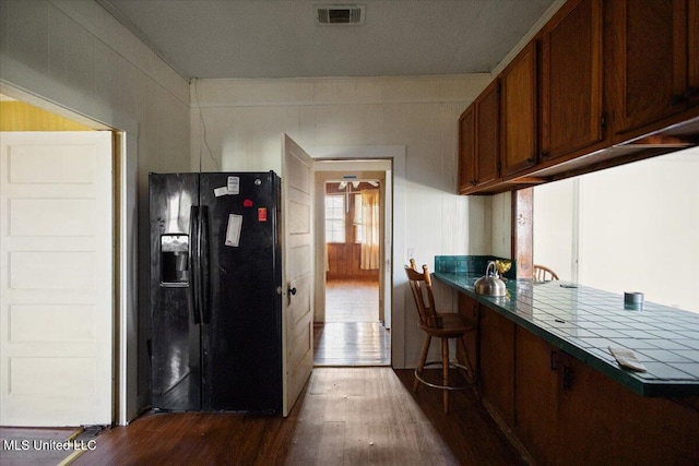 kitchen with dark wood-style floors, visible vents, a kitchen bar, brown cabinets, and black refrigerator with ice dispenser