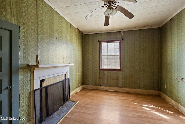 unfurnished living room featuring crown molding, ceiling fan, baseboards, a fireplace with flush hearth, and wood finished floors