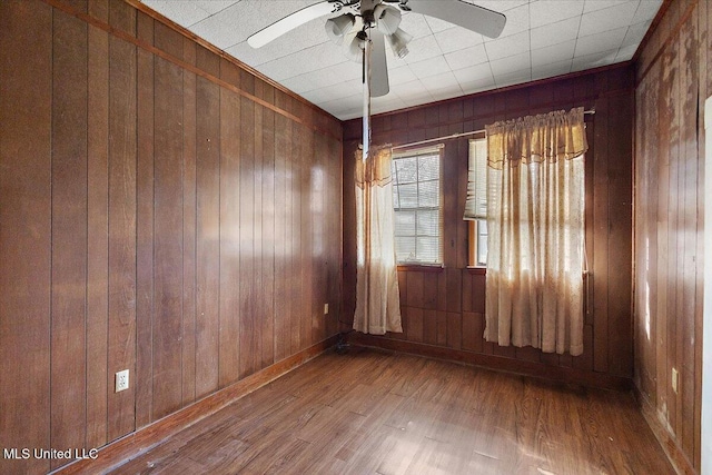 empty room with ceiling fan, wood finished floors, and wood walls