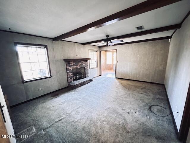 unfurnished living room with beamed ceiling, ceiling fan, dark colored carpet, and a brick fireplace