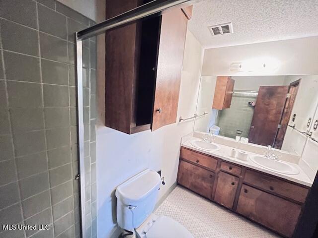 bathroom with tile patterned flooring, a textured ceiling, toilet, vanity, and a shower with shower door