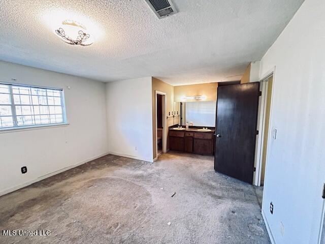 unfurnished bedroom featuring a textured ceiling, light colored carpet, and connected bathroom