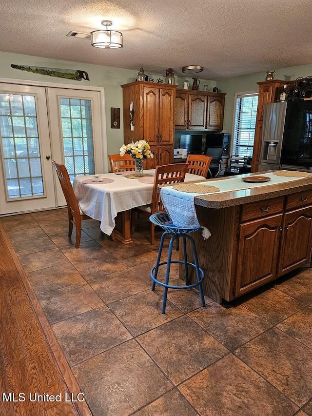 kitchen with stainless steel refrigerator with ice dispenser, a textured ceiling, plenty of natural light, and a kitchen breakfast bar