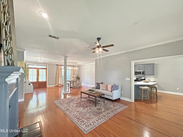 living room with ornate columns, light hardwood / wood-style floors, ceiling fan with notable chandelier, and ornamental molding