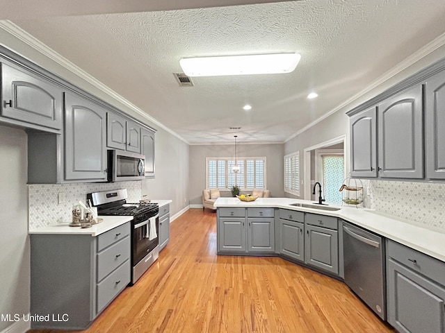 kitchen with ornamental molding, gray cabinetry, stainless steel appliances, sink, and hanging light fixtures