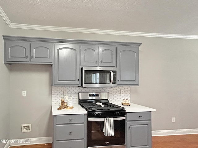 kitchen with appliances with stainless steel finishes, backsplash, dark hardwood / wood-style floors, and gray cabinetry