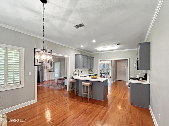 kitchen with ornamental molding, gray cabinetry, decorative light fixtures, light hardwood / wood-style floors, and a breakfast bar area