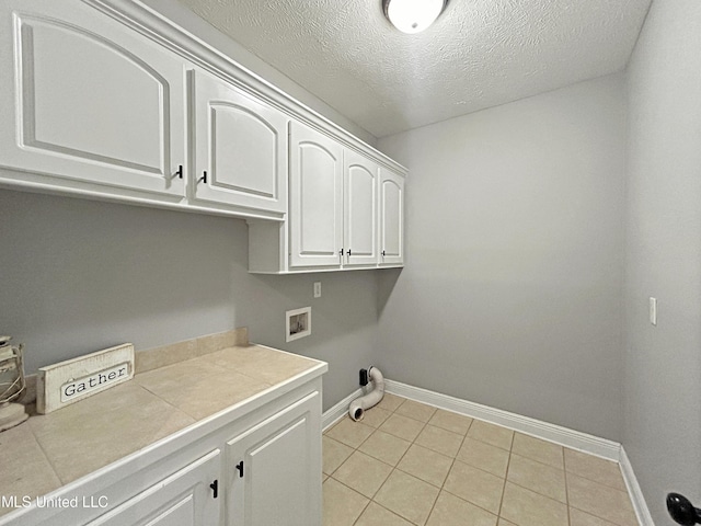 laundry room featuring cabinets, hookup for a washing machine, a textured ceiling, and light tile patterned floors