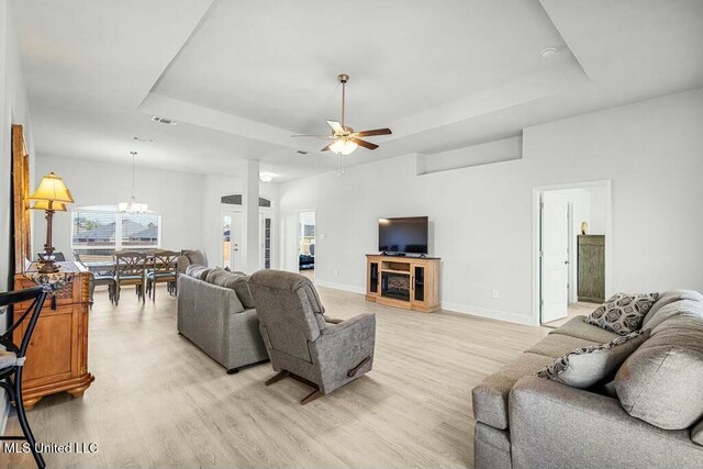 living room featuring ceiling fan with notable chandelier, light hardwood / wood-style floors, and a raised ceiling