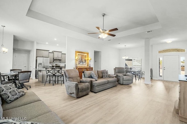 living room featuring a tray ceiling, ceiling fan with notable chandelier, and light hardwood / wood-style flooring