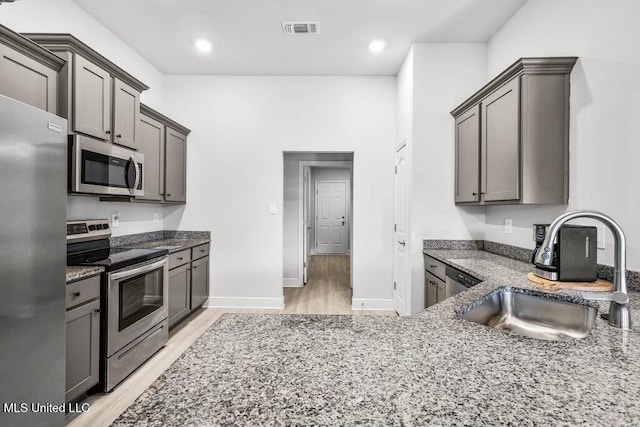 kitchen featuring light hardwood / wood-style floors, stainless steel appliances, stone countertops, and sink