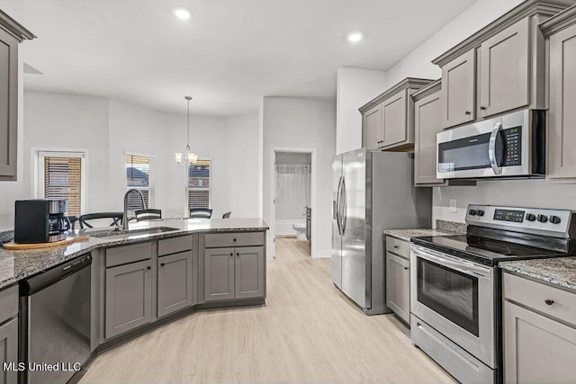 kitchen with sink, gray cabinets, appliances with stainless steel finishes, light stone countertops, and decorative light fixtures