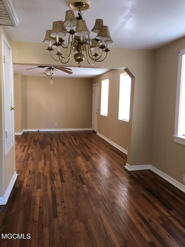 unfurnished dining area featuring ceiling fan with notable chandelier, dark hardwood / wood-style floors, and a healthy amount of sunlight