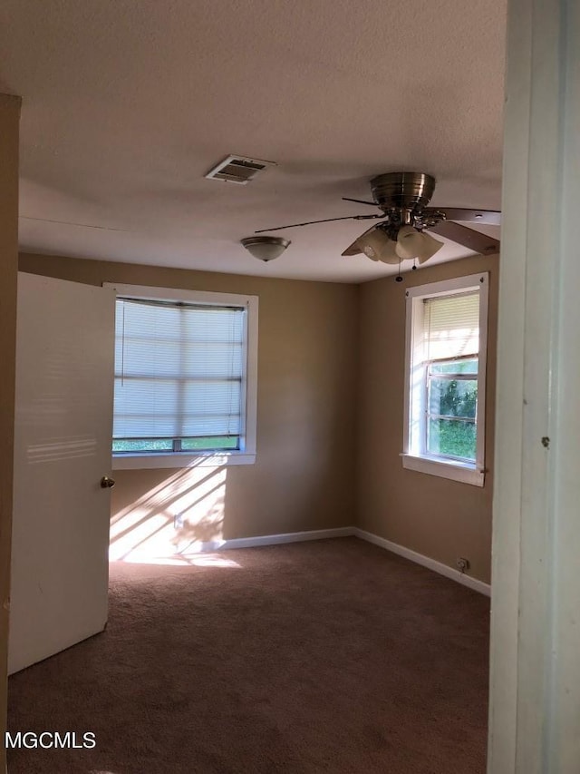 unfurnished room with a textured ceiling, ceiling fan, and dark colored carpet