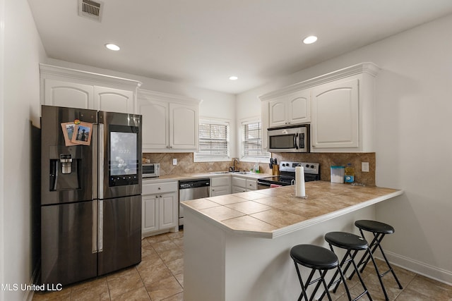 kitchen featuring visible vents, a kitchen breakfast bar, white cabinetry, stainless steel appliances, and a peninsula