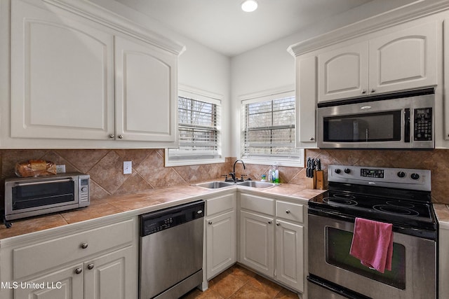 kitchen with tile countertops, a sink, decorative backsplash, appliances with stainless steel finishes, and white cabinetry