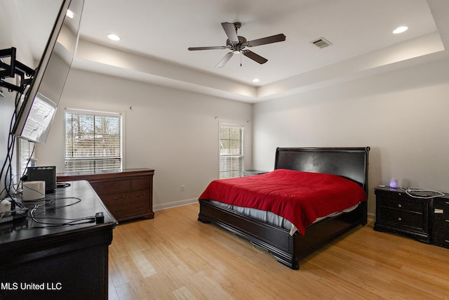 bedroom with a tray ceiling, multiple windows, visible vents, and light wood finished floors