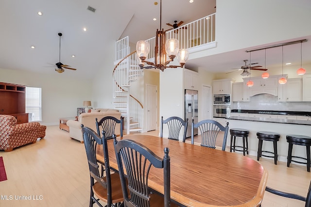 4013 Haiti St, Bay Saint Louis, MS 39520 - dining area featuring light wood-type flooring, visible vents, ceiling fan with notable chandelier, stairway, and high vaulted ceiling