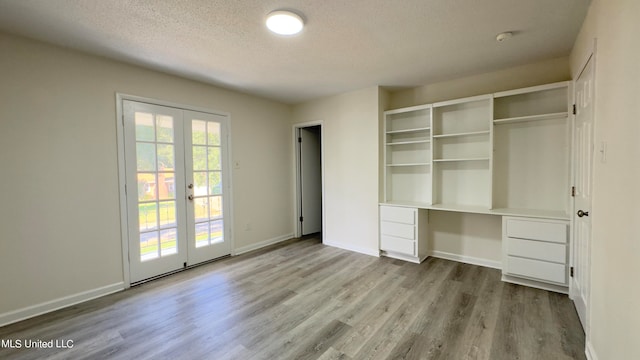 unfurnished bedroom with french doors, a textured ceiling, and light hardwood / wood-style flooring