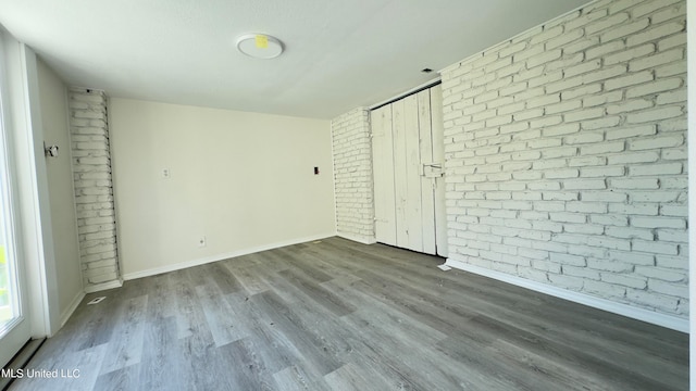 unfurnished bedroom with hardwood / wood-style floors and brick wall