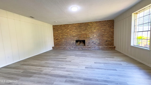 unfurnished living room featuring light hardwood / wood-style flooring, brick wall, plenty of natural light, and a brick fireplace