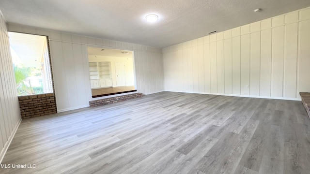 unfurnished room featuring built in features, a textured ceiling, and light hardwood / wood-style flooring