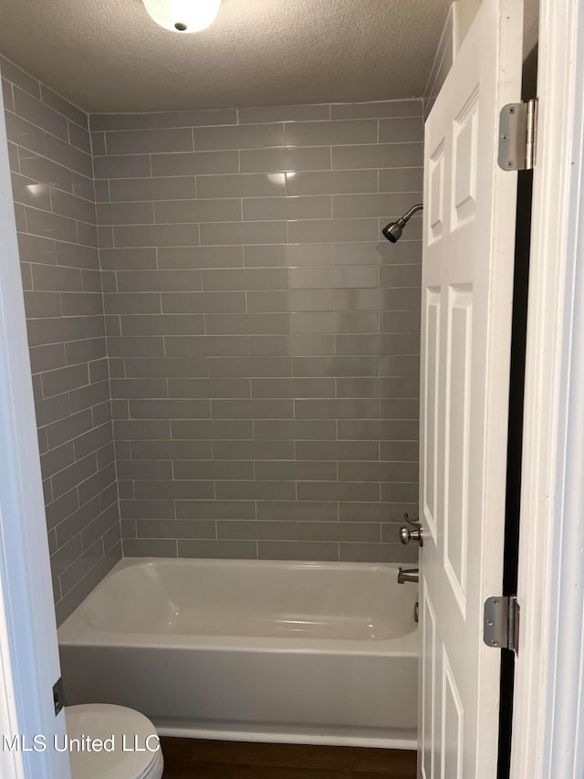 bathroom with tiled shower / bath, a textured ceiling, and toilet