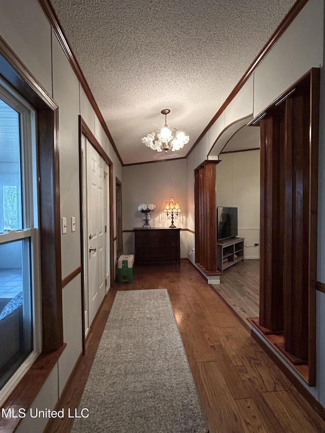 hall featuring a notable chandelier, hardwood / wood-style flooring, a textured ceiling, and ornamental molding