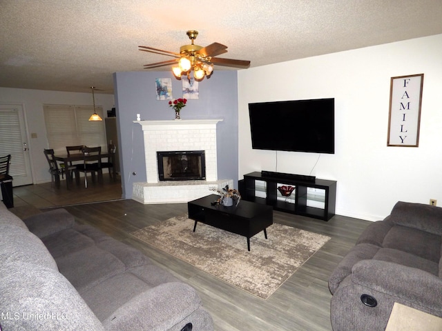 living room featuring ceiling fan, a fireplace, dark hardwood / wood-style floors, and a textured ceiling