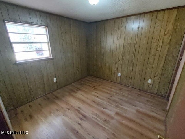 unfurnished room with wood walls and light hardwood / wood-style floors